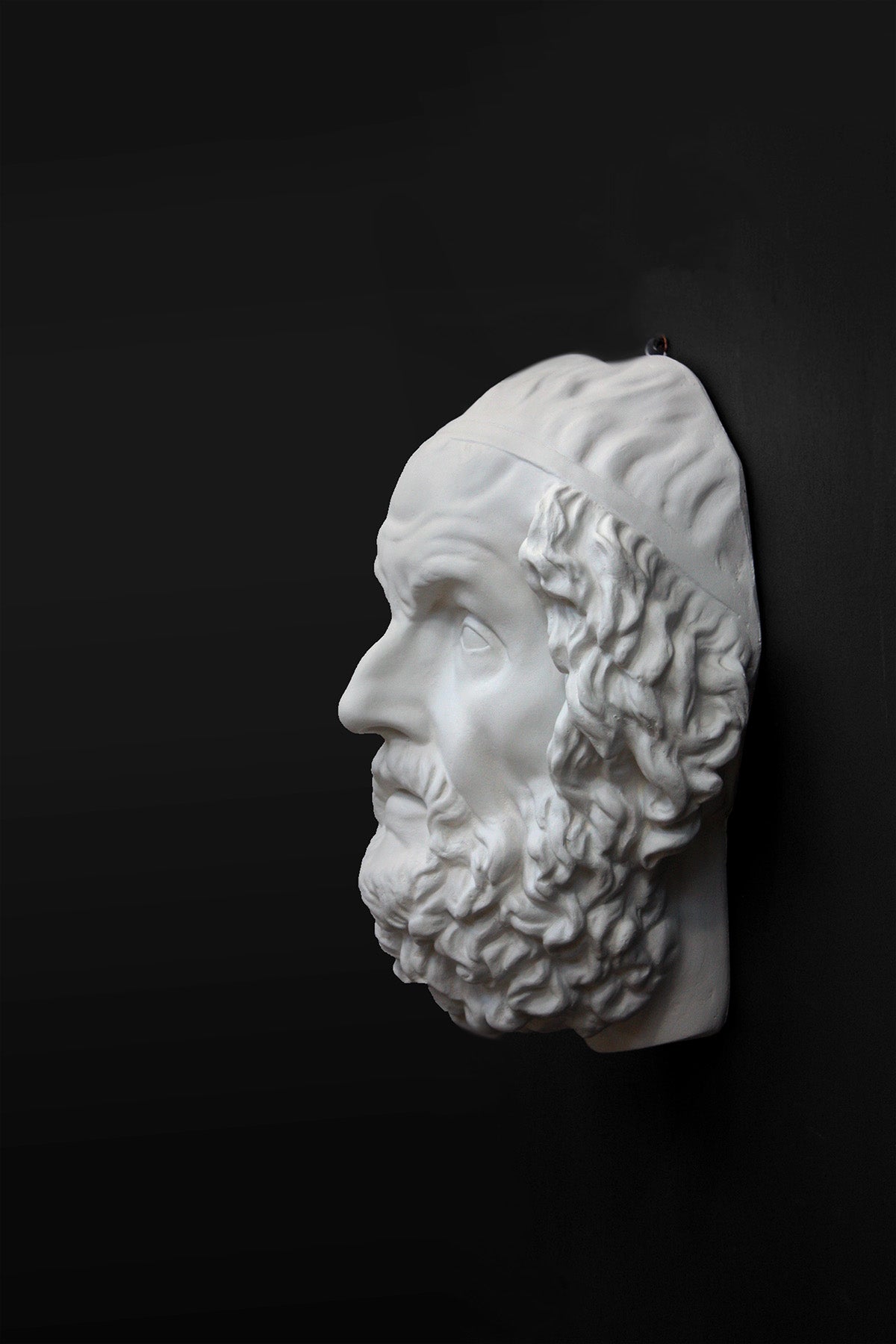 Photo of a white plaster cast mask from a sculpture of Homer on a black background