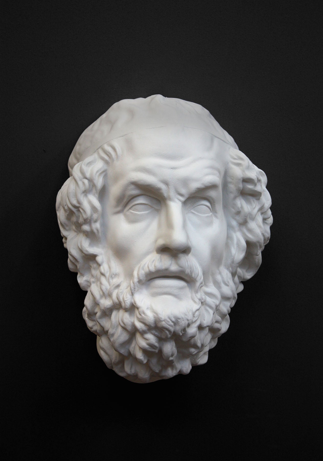 Photo of a white plaster cast mask from a sculpture of Homer on a black background