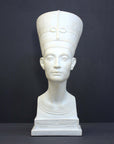 photo of plaster cast sculpture of bust of Nefertiti with crown and decorative collar on a decorative base with a black background