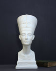photo of plaster cast sculpture of bust of Nefertiti with crown and decorative collar on a decorative base with a black background