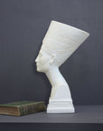 photo of plaster cast sculpture of bust of Nefertiti with crown and decorative collar on a decorative base with a black background