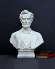 image of a plaster sculpture bust of man, namely Abraham Lincoln, next to stacked green and red books on a gray background
