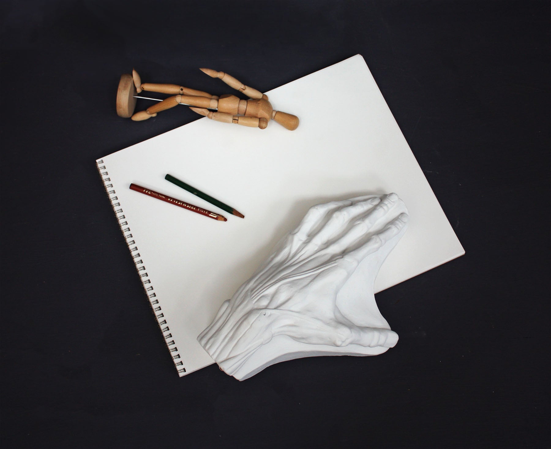 Photo of a plaster cast of a flayed hand for artist study on the top of a drawing pad with pencils and a wooden figure