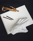Photo of a plaster cast of a flayed hand for artist study on the top of a drawing pad with pencils and a wooden figure