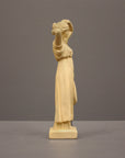 photo of off-white plaster cast statue of a female in robes with her arms raised to her head against gray background
