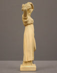 photo of off-white plaster cast statue of a female in robes with her arms raised to her head against gray background