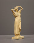 photo of off-white plaster cast statue of a female in robes with her arms raised to her head against gray background