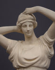 detail photo of off-white plaster cast statue of a female in robes with her arms raised to her head against gray background