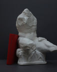 image of a plaster sculpture of nude male torso next to a red book on a gray background