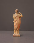 photo of plaster cast statue of female in pink robes with left arm raised and holding robe on gray background