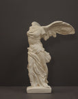 photo of plaster cast sculpture of winged, headless female figure with flowing drapery on a gray background
