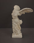 photo of plaster cast sculpture of winged, headless female figure with flowing drapery on a gray background