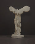 photo of plaster cast sculpture of winged, headless female figure with flowing drapery on a gray background