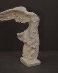 photo of plaster cast sculpture of winged, headless female figure with flowing drapery on a gray background