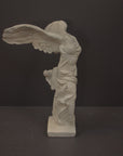 photo of plaster cast sculpture of winged, headless female figure with flowing drapery on a gray background