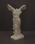 photo of plaster cast sculpture of winged, headless female figure with flowing drapery on a gray background