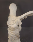 detail photo of plaster cast sculpture of winged, headless female figure with flowing drapery on a gray background
