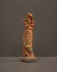 photo of plaster cast statue of a female in pink-orange tinted robes with her arms raised to her head against gray background