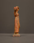 photo of plaster cast statue of a female in pink-orange tinted robes with her arms raised to her head against gray background