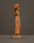 photo of plaster cast statue of a female in pink-orange tinted robes with her arms raised to her head against gray background