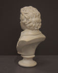 back view image of a plaster sculpture bust of man, namely Mozart, with ruffled necktie and coat on a gray background