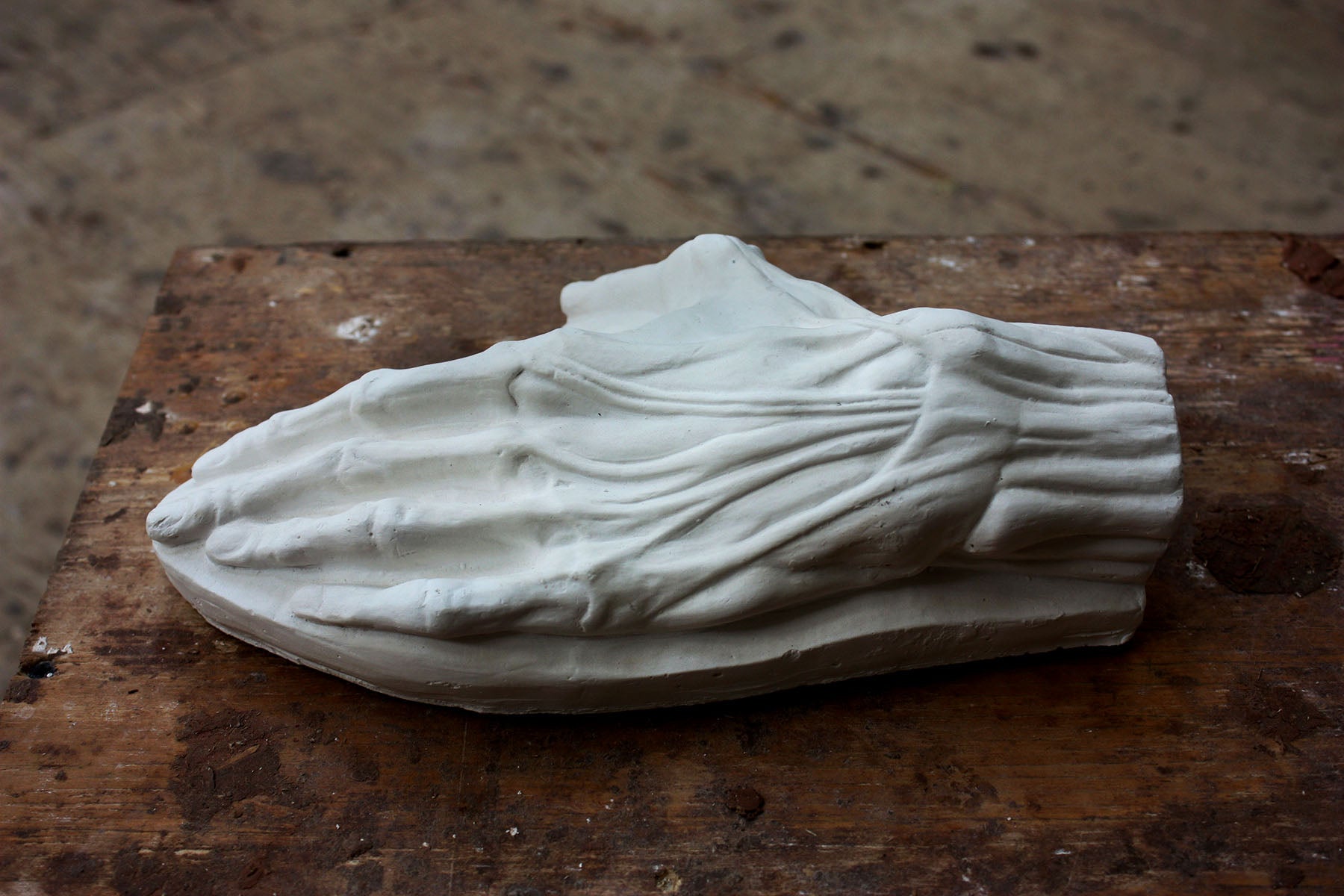 Photo of a plaster cast of a flayed hand for artist study on a wooden table with paint splatters