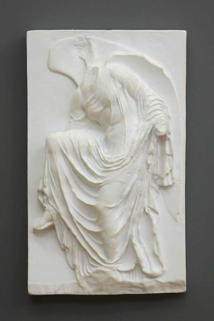 photo of cast of sculpture relief of robed figure, head now missing, reaching for her sandal on a dark gray background