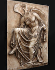 photo of cast of sculpture relief of robed figure, head now missing, reaching for her sandal in a brown patina on a dark gray background
