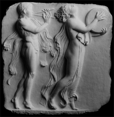 Photo of white plaster cast relief sculpture of two figures dancing in a procession against a black background