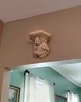 photo of plaster cast sculpture of architectural bracket featuring a man's upper body who holds a musical instrument, affixed to beige wall above doorway to room with green walls and curtains