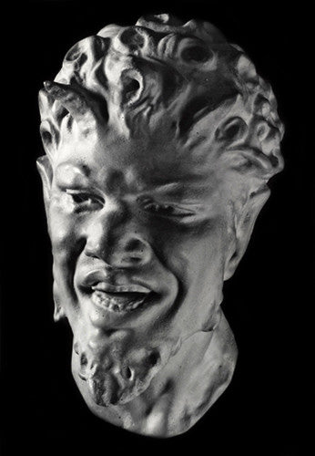 photo with black background of plaster cast sculpture of male faun head with curly hair, horns, beard and open mouth