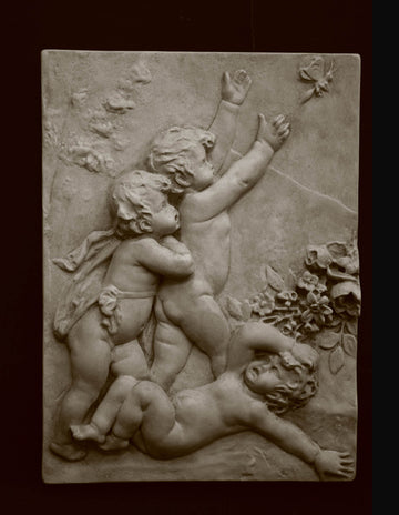photo with black background of plaster cast relief sculpture of three cupids, two close together chasing a butterfly and one on ground