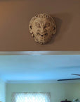 photo of plaster cast sculpture of grotesque faun face, affixed to beige wall above doorway to room with light walls and ceiling fan