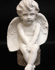 image of plaster sculpture of seated angel on a black background