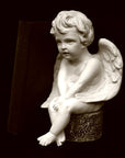 image of plaster sculpture of seated angel with red book beside it on a black background