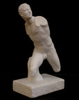 photo of white plaster cast sculpture of male figure in active pose without arms or lower legs on a base against black background