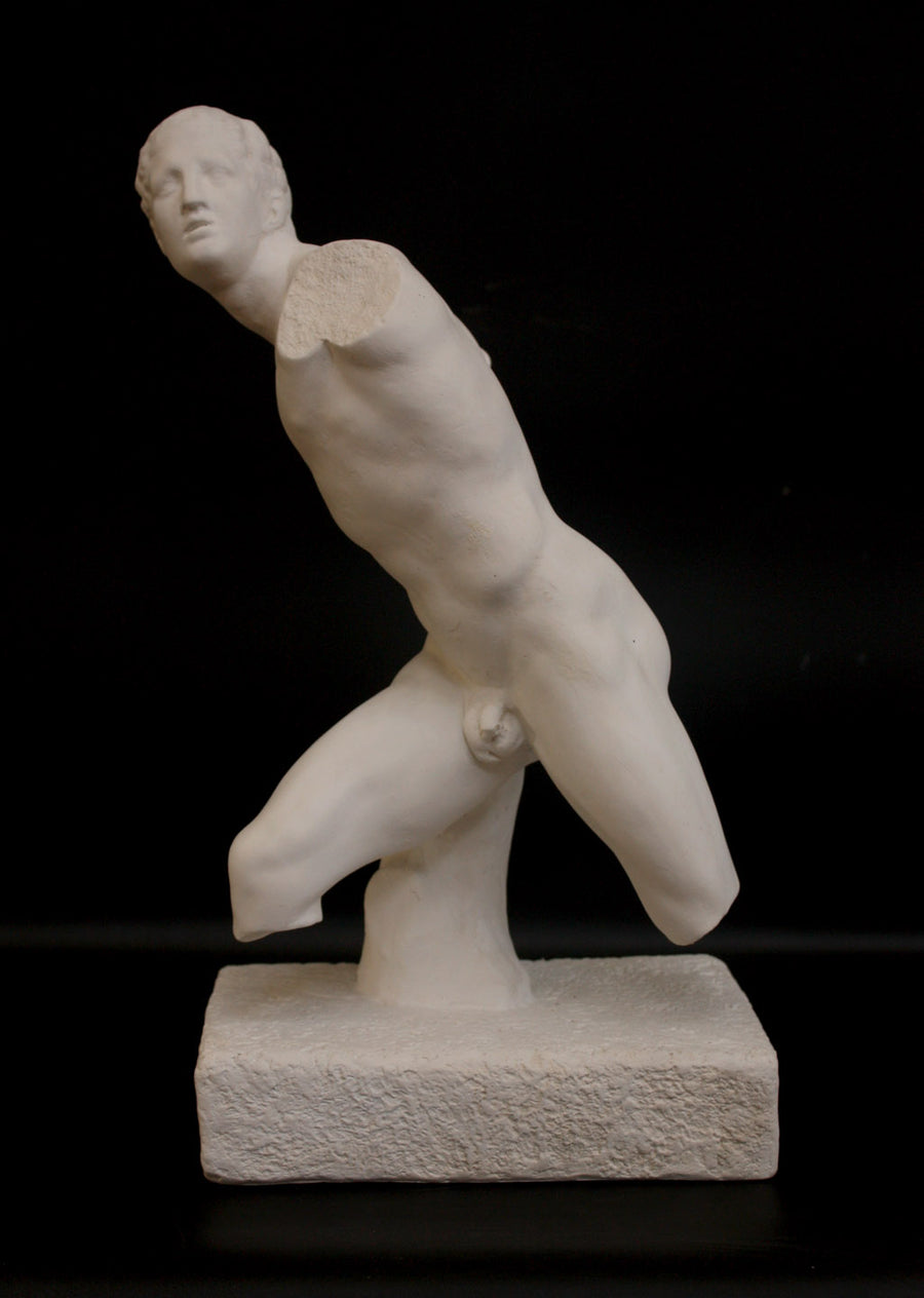 photo of white plaster cast sculpture of male figure in active pose without arms or lower legs on a base against black background