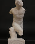 photo of white plaster cast sculpture of male figure in active pose without arms or lower legs on a base against black background