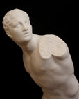 closeup photo of white plaster cast sculpture of male figure in active pose without arms or lower legs on a base against black background