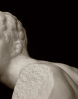 closeup photo of white plaster cast sculpture of male figure in active pose without arms or lower legs on a base against black background