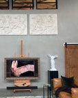 photo of white plaster cast sculpture of winged, headless female figure with flowing drapery against gray wall beside swan photo and wood door and foreground with leather furniture