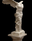 photo of plaster cast sculpture of winged, headless female figure with flowing drapery on top of a Doric-column pedestal on a black background