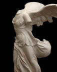 photo of plaster cast sculpture of winged, headless female figure with flowing drapery on a black background