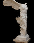 photo of plaster cast sculpture of winged, headless female figure with flowing drapery on top of an ornate, floral pedestal on a black background