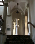 photo of plaster cast sculpture of winged, headless female figure with flowing drapery on pedestal atop a carpeted staircase in a niche in a white-walled room