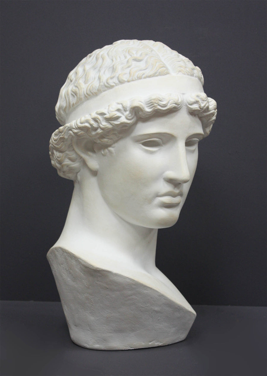photo of white plaster cast sculpture bust of female, namely the goddess Athena, with short, curly hair and headband on gray background