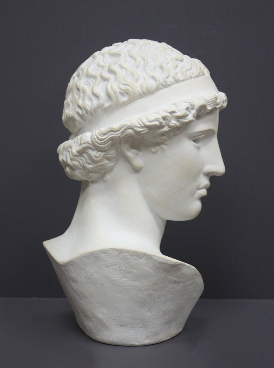 photo of white plaster cast sculpture bust of female, namely the goddess Athena, with short, curly hair and headband on gray background