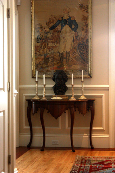 photo of bronze-colored plaster cast sculpture bust of man, namely Beethoven, with neckerchief on dark wood table with candlesticks and portrait painting behind