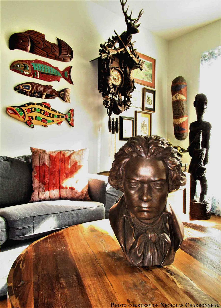 photo of bronze-colored plaster cast sculpture bust of man, namely Beethoven, with neckerchief on wooden table in room with various collectibles