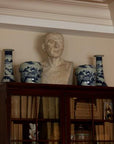 photo of plaster cast sculpture of male head of Cicero with squared bust and white and blue vases on a dark wood bookcase against a tan wall and staircase railing to the left